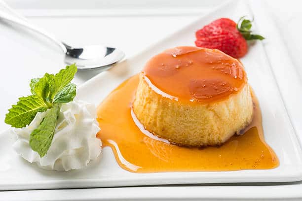 Flan coco-caramel dans une assiette à dessert avec de la chantilly et des fraises