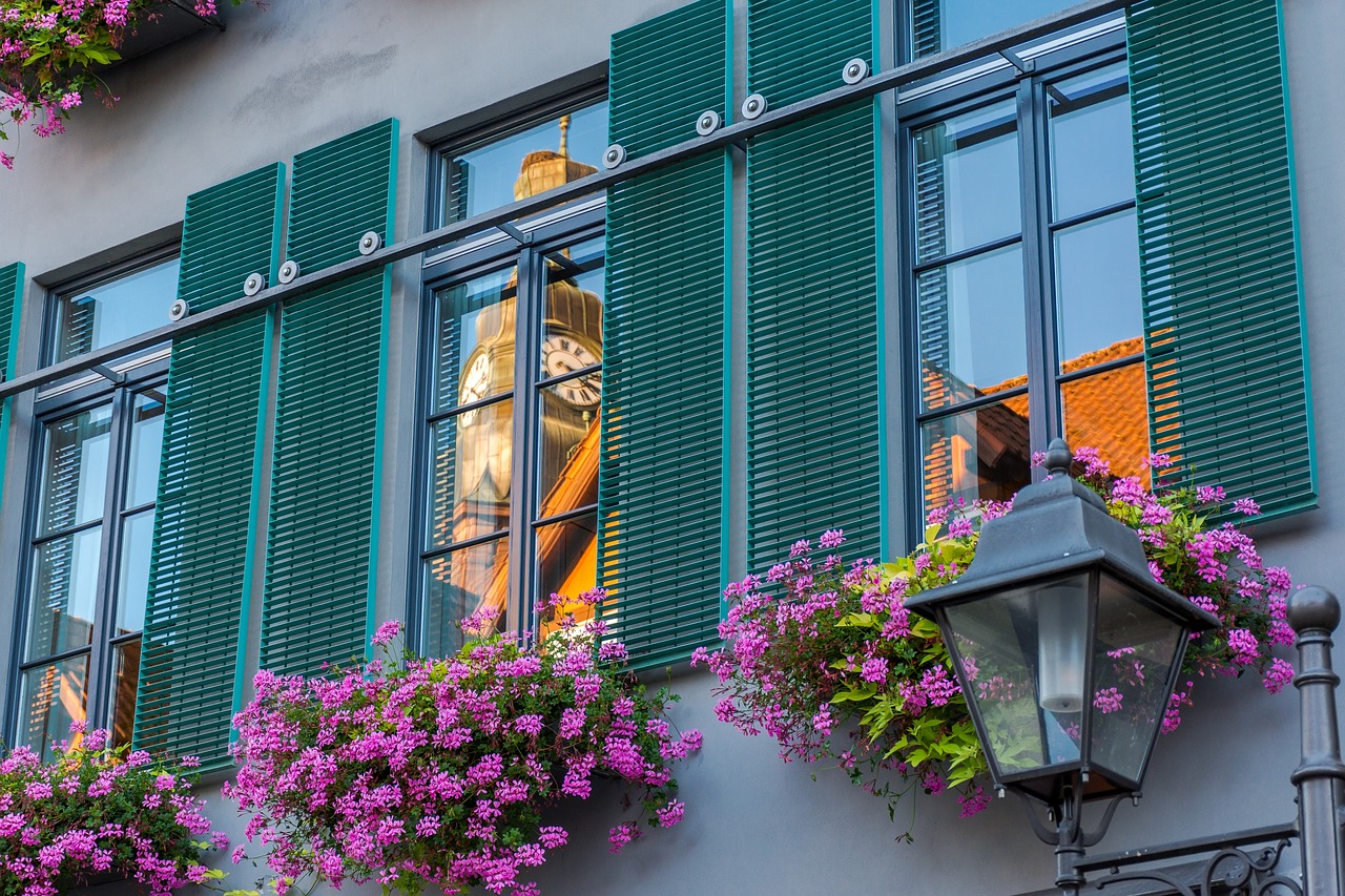 façade avec fenêtres aux volets verts et jardinières de fleurs roses