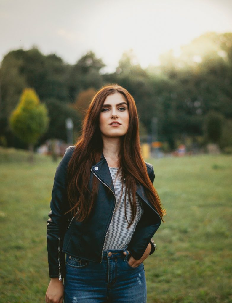 femme aux cheveux longs portant une veste en cuir noir et un pull gris avec un jean