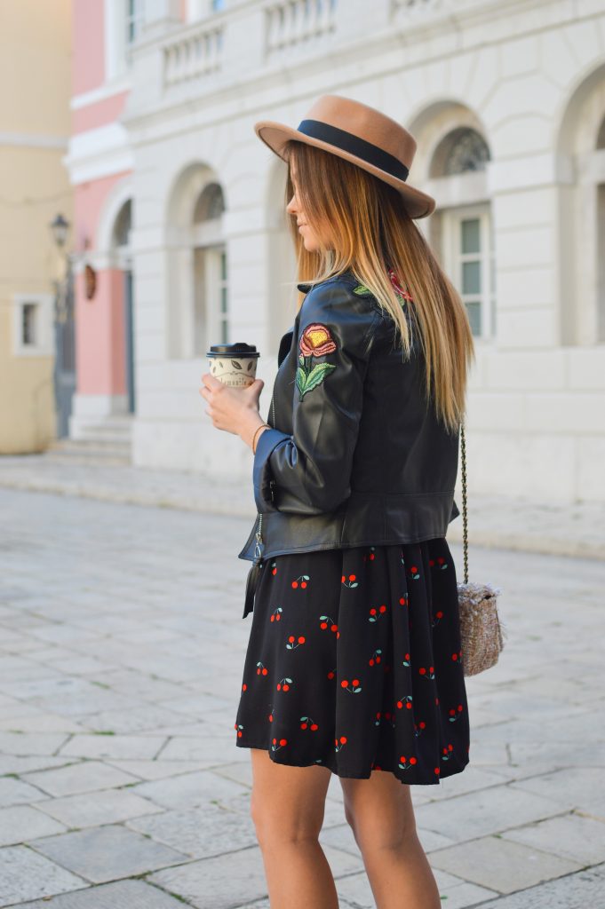 femme blonde aux cheveux longs portant une veste en cuir noir sur une robe courte noire avec un motif cerises