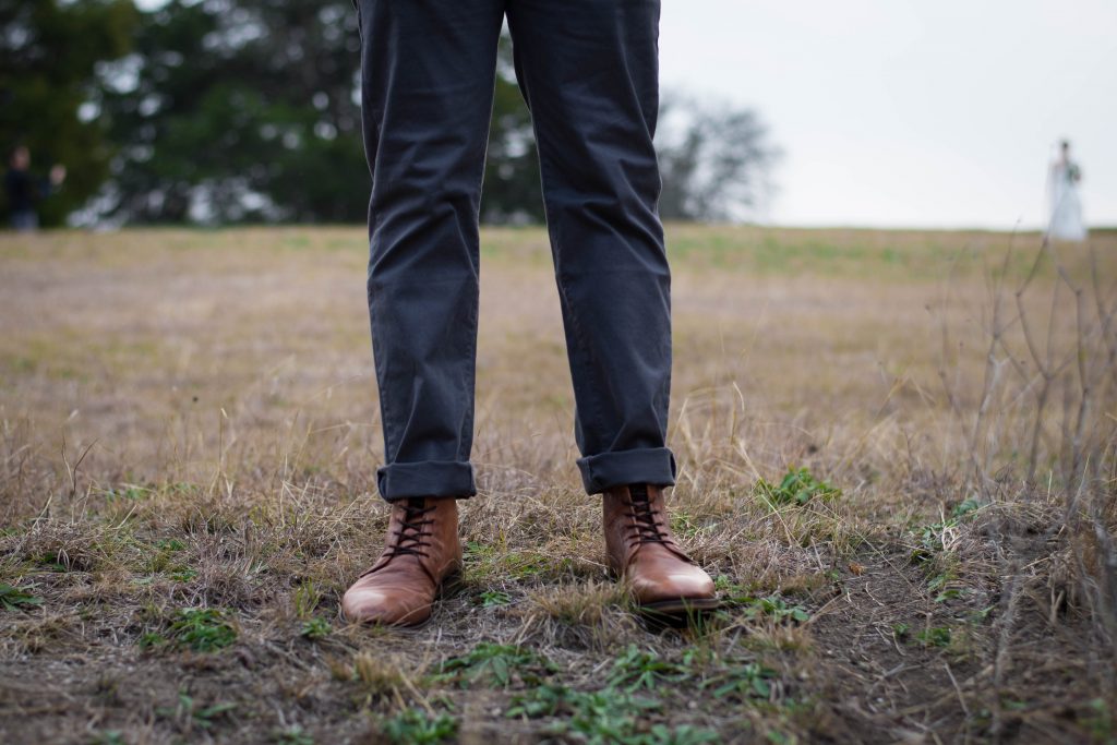 jambes d'un homme portant un pantalon sombre et des bottines à lacets marron