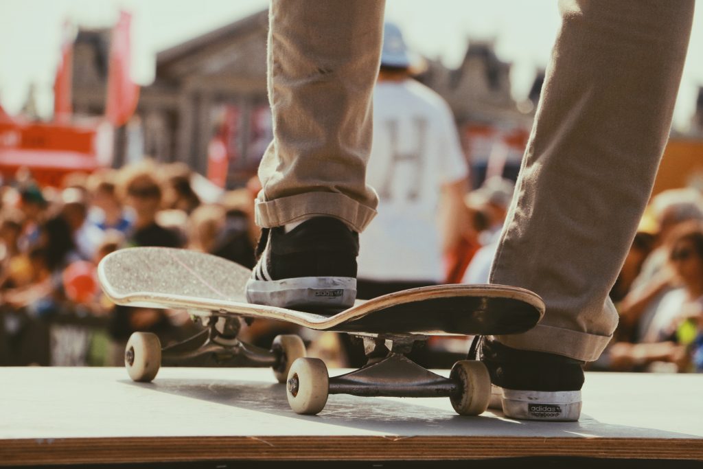 bas des jambes d'un homme portant un pantalon chino beige des baskets noires et blanches avec un pied sur un skate