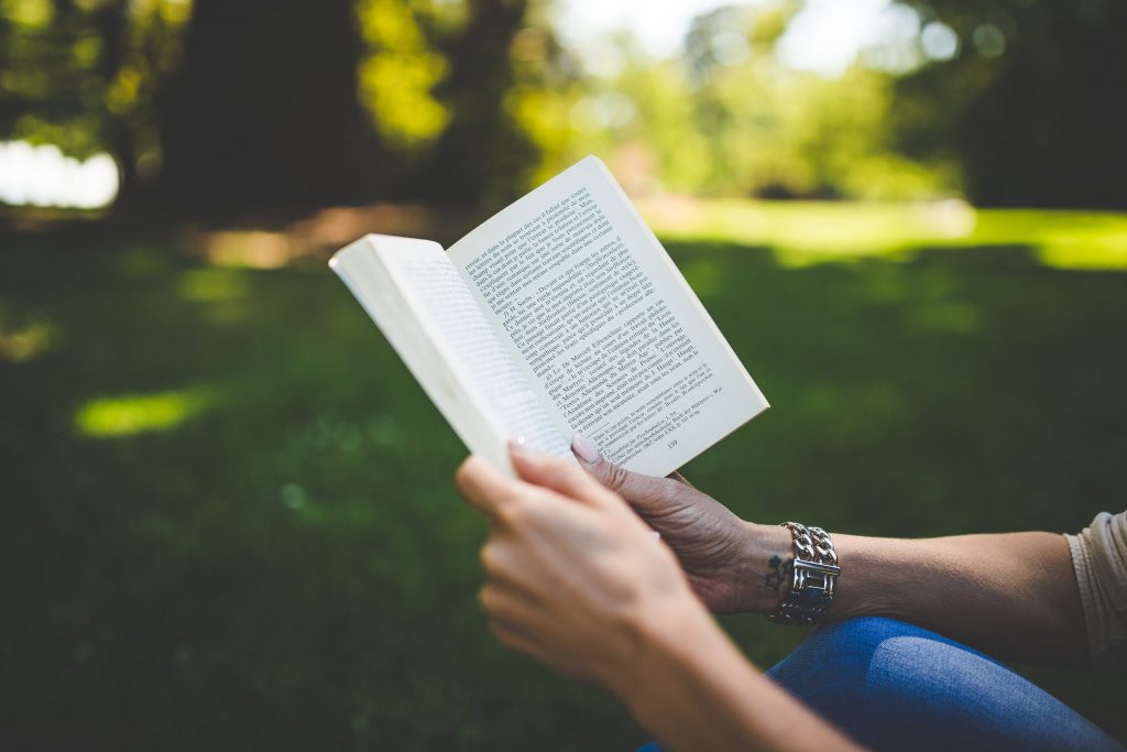 Jeune femme qui lit un livre young adult de fantasy dans un parc